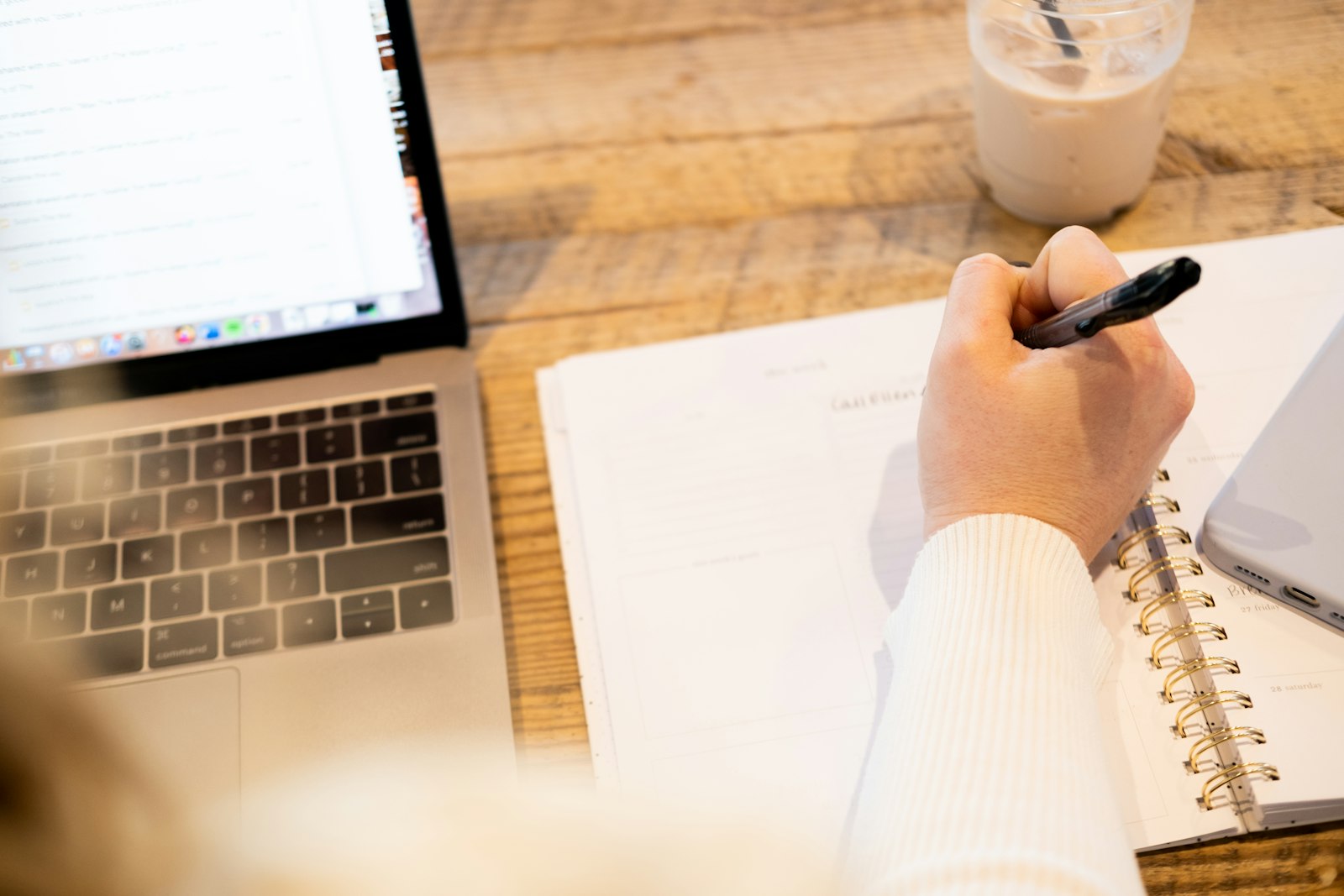 Person macht Notizen am Schreibtisch neben dem Laptop