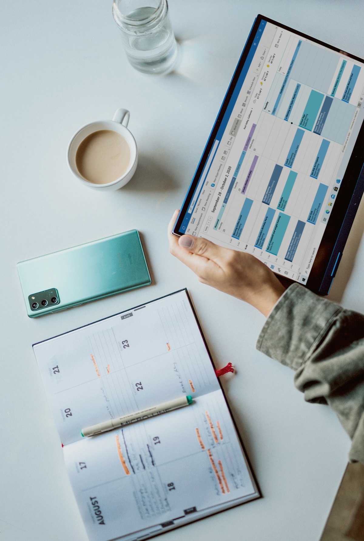 Person hält Tablet mit digitalem Wochenkalender, daneben aufgeschlagener Papierplaner — Personalplanung digital und analog